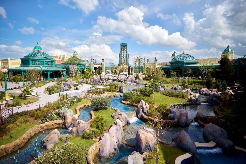 A wide shot of winding rivers and green grassy gardens leading up to turquoise domes and towers. 