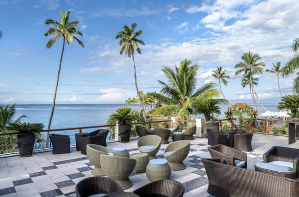 Outdoor seating area with ocean view and palm trees at Warwick Fiji Resort and Spa.