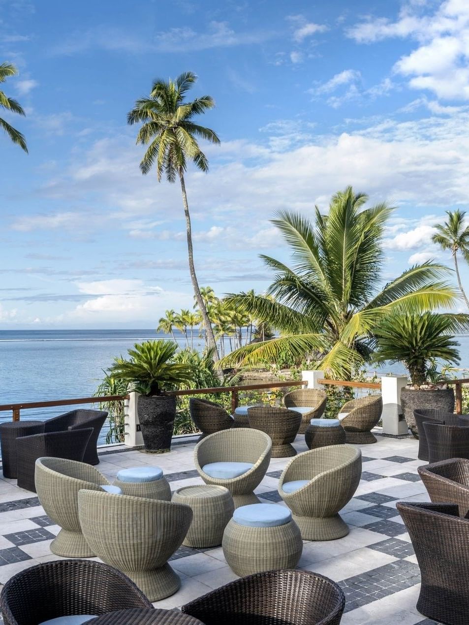 Woven chairs by a stone railing under palm trees in Sunset Terrace Bar at Warwick Fiji Resort and Spa