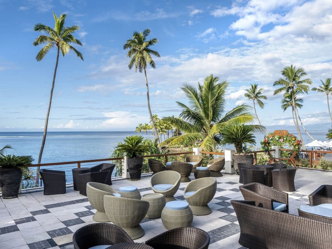 Woven chairs by a stone railing under palm trees in Sunset Terrace Bar at Warwick Fiji Resort and Spa