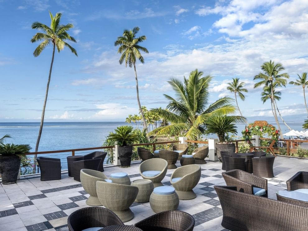 Woven chairs by a stone railing under palm trees in Sunset Terrace Bar at Warwick Fiji Resort and Spa