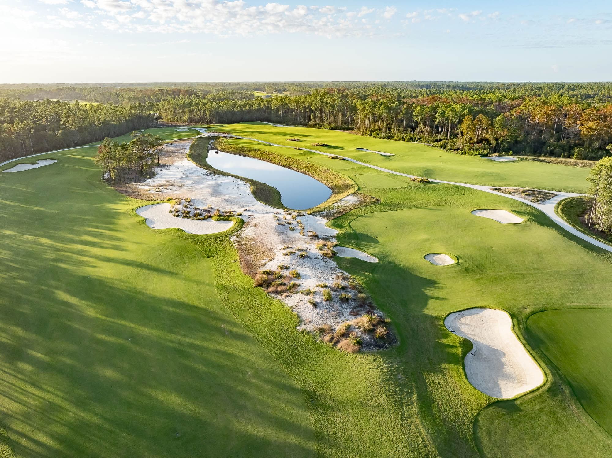 Aerial view of a golf course with green fairways, sand traps, and a central water feature.