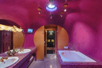Modern bathroom with vibrant pink walls, elegant fixtures, double sinks, a bathtub, and a TV at The Roxbury