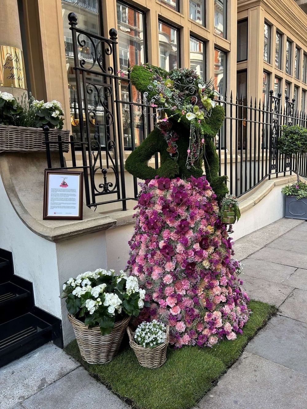 Floral sculpture and baskets outside building with black gates and white walls.