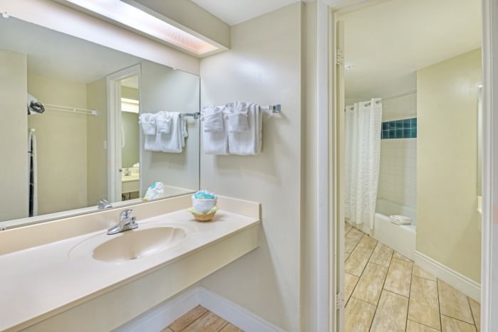 A bathroom with a sink, mirror, and towels, with a shower visible in the background.