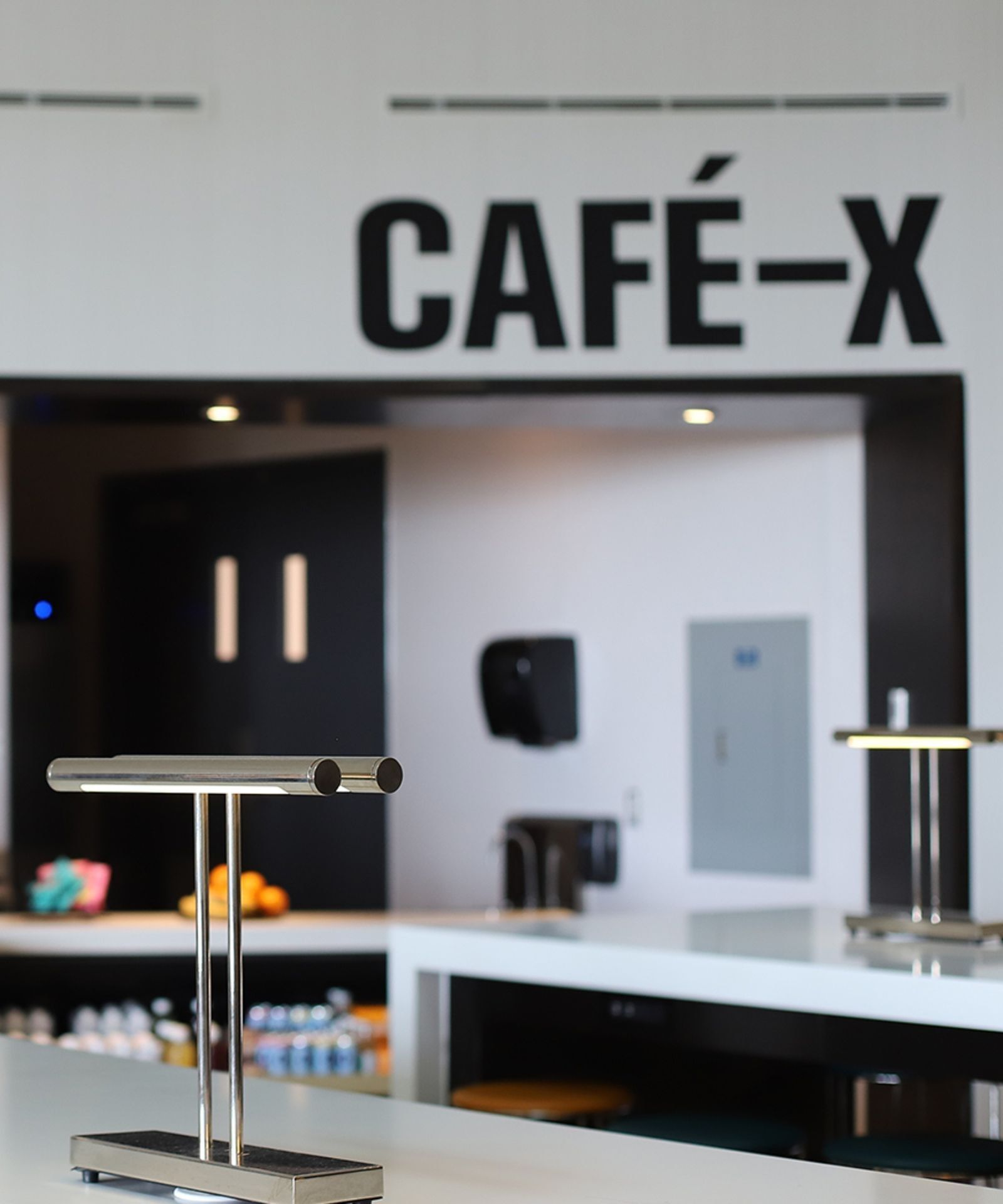 Cafe-X counter with serving lamps and refreshments displayed beneath bold signage in modern interior at Hotel X Toronto