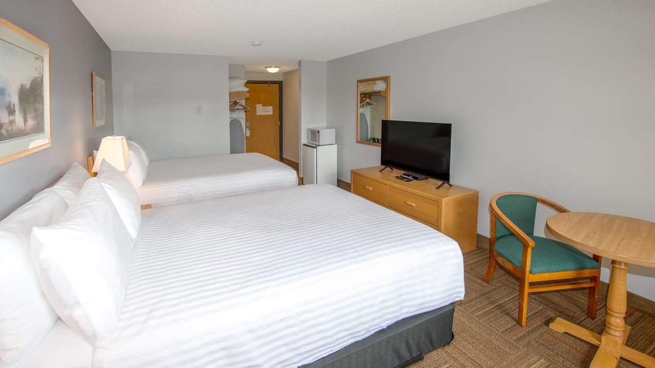 Two beds, TV, chair, and table in a hotel room with gray walls.