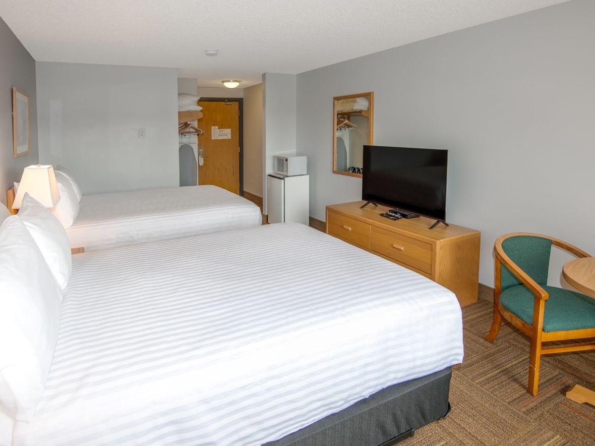 Two beds, nightstands, TV, chair, and small table in a hotel room.