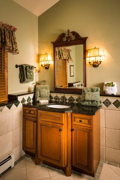 A bathroom with a wooden vanity, a large framed mirror with two sconces, and green towels at The Stanley Hotel