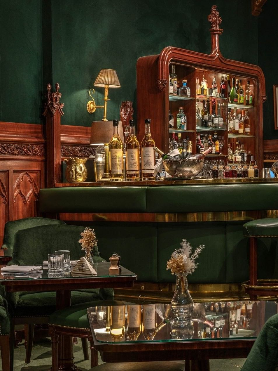 Duke's Bar bar area with green velvet armchairs by glass tables under a dark wooden bar counter at Hotel Westminster Paris