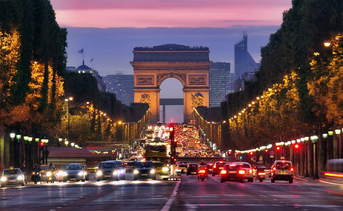 Arc de Triomphe by city traffic under a purple sunset, surrounding trees near Warwick Paris Champs Elysées