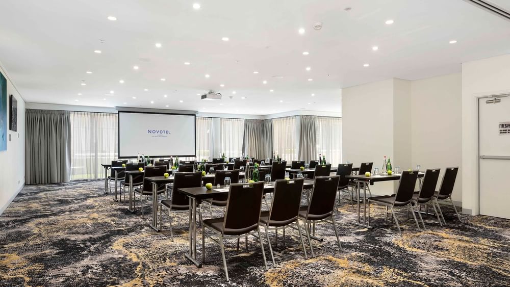 Classroom set-up with a projector screen and carpeted floors in The Barossa Room at Novotel Sydney on Darling Harbour