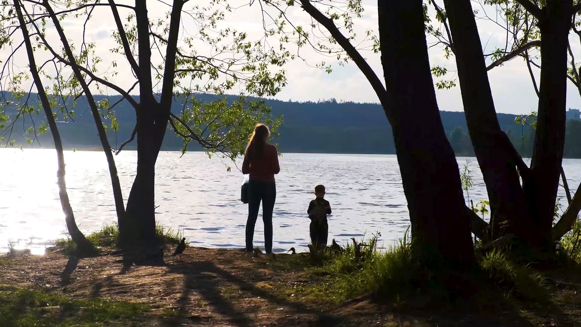 Mother and son standing by a lake, surrounded by trees, enjoying a peaceful moment near Coast Penticton Hotel
