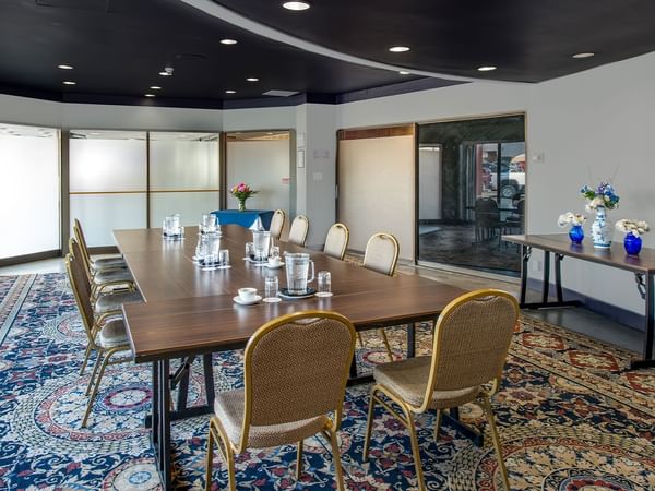 Meeting room with a long table, chairs, and floral vases, set on a patterned carpet.