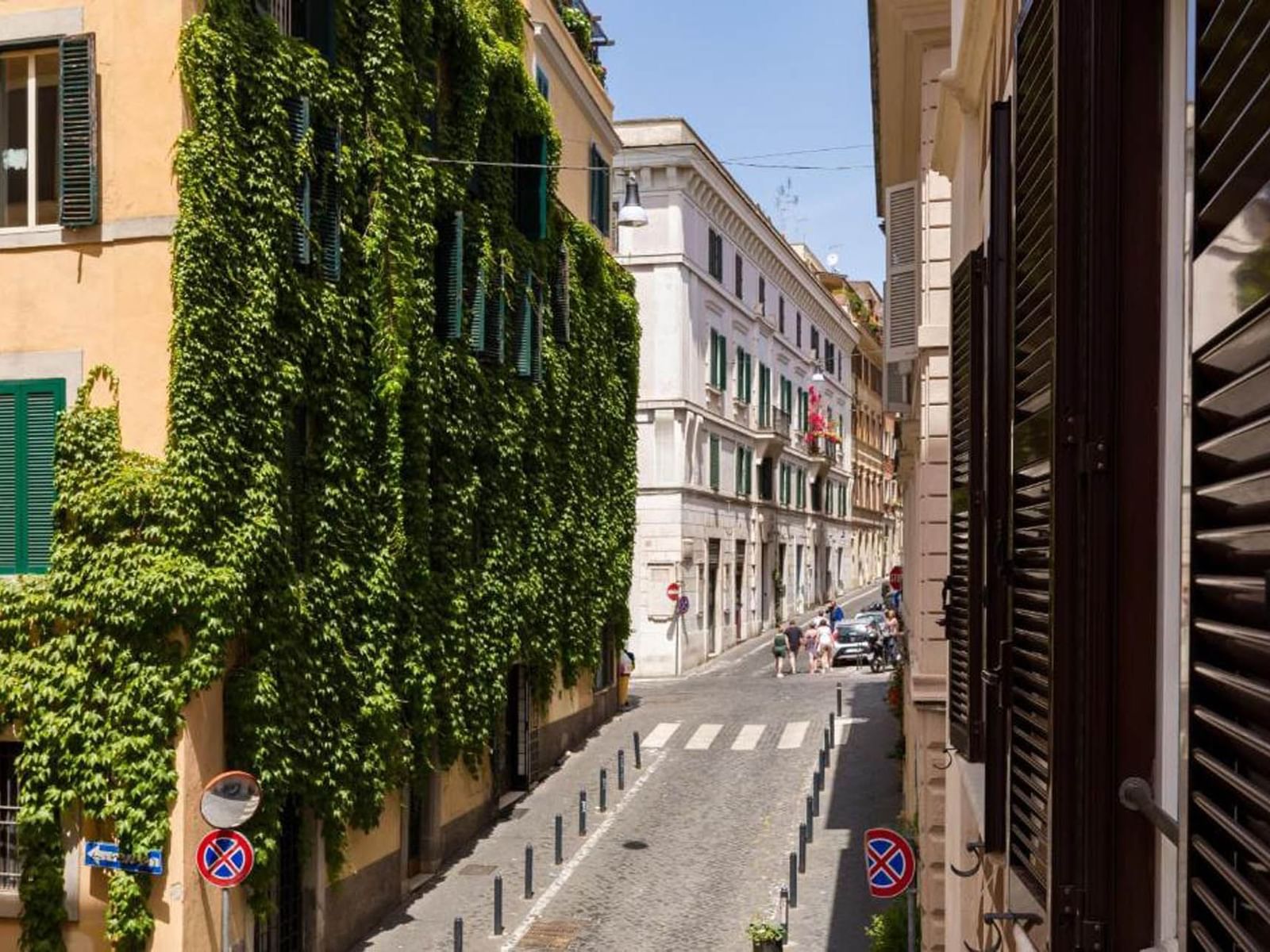 Via del Boschetto street lined with greenery, featuring cobblestone pavement and people walking near The Glam Hotel