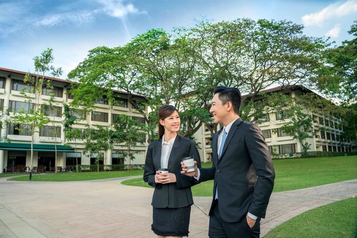 Man and a woman chatting outdoors with coffee, surrounded by greenery and a building at The Saujana Hotel Kuala Lumpur