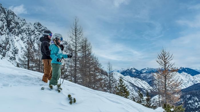 Two skiers standing on a snowy hill with a mountain view near Falkensteiner Hotel and Spa Carinzia