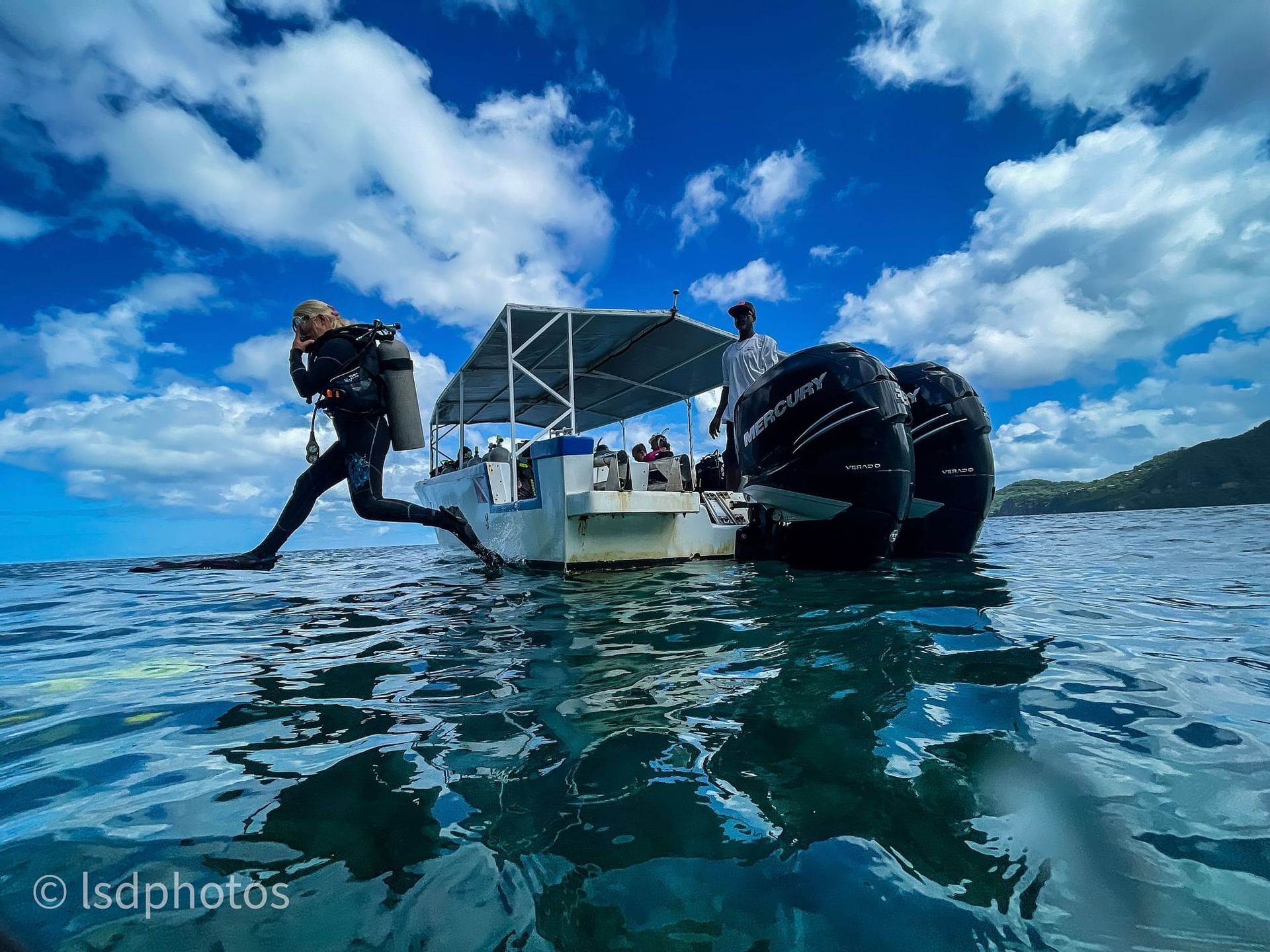 Diver in a wetsuit jumping off a boat into clear blue water under a vibrant sky near Bay Gardens Hotels and Resorts