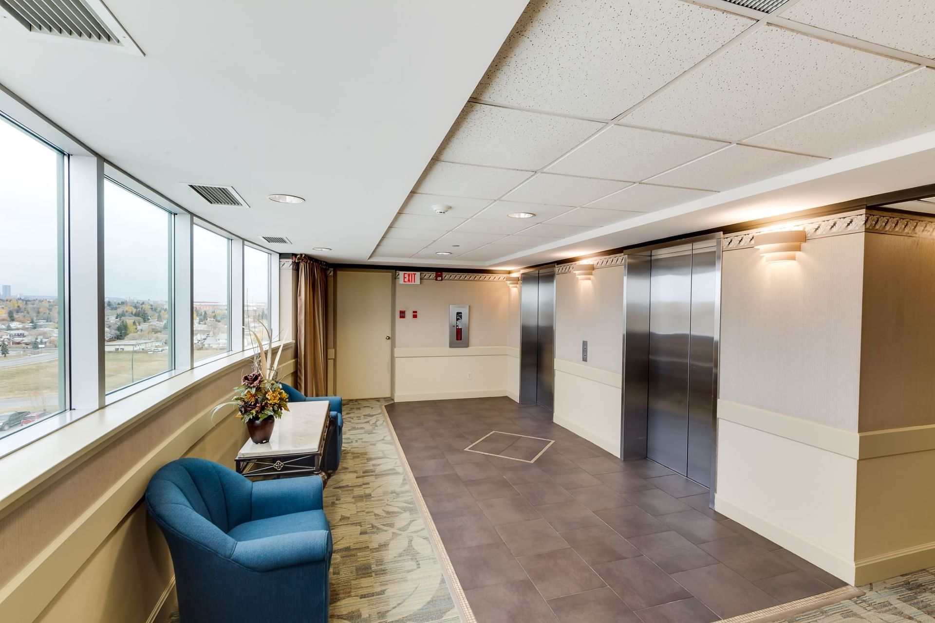 Elevator lobby with blue armchairs by a window, floral centerpiece under wall sconces at The Glenmore Inn