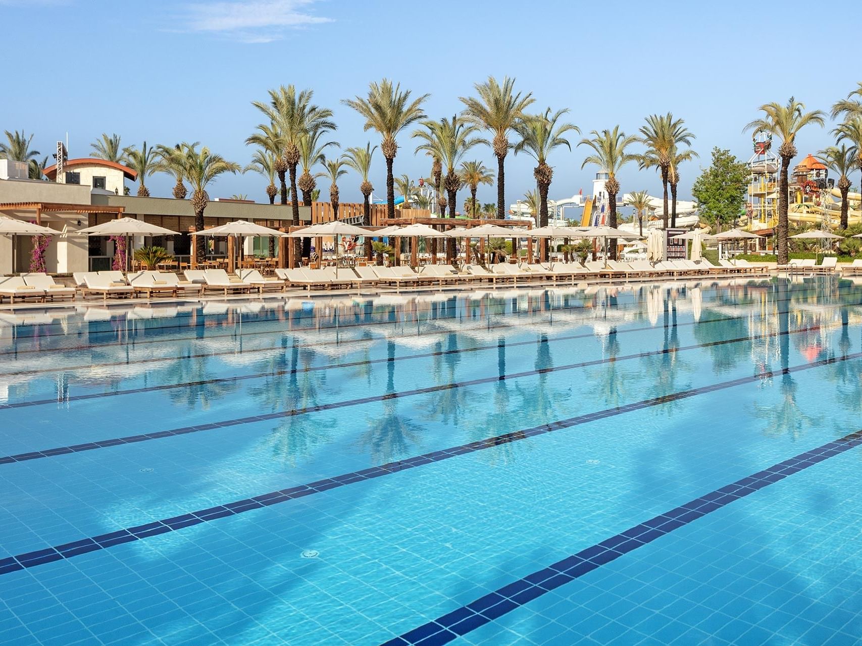 Sun loungers lined-up under sun huts by Olympic Pool at Titanic Deluxe Lara on a sunny day
