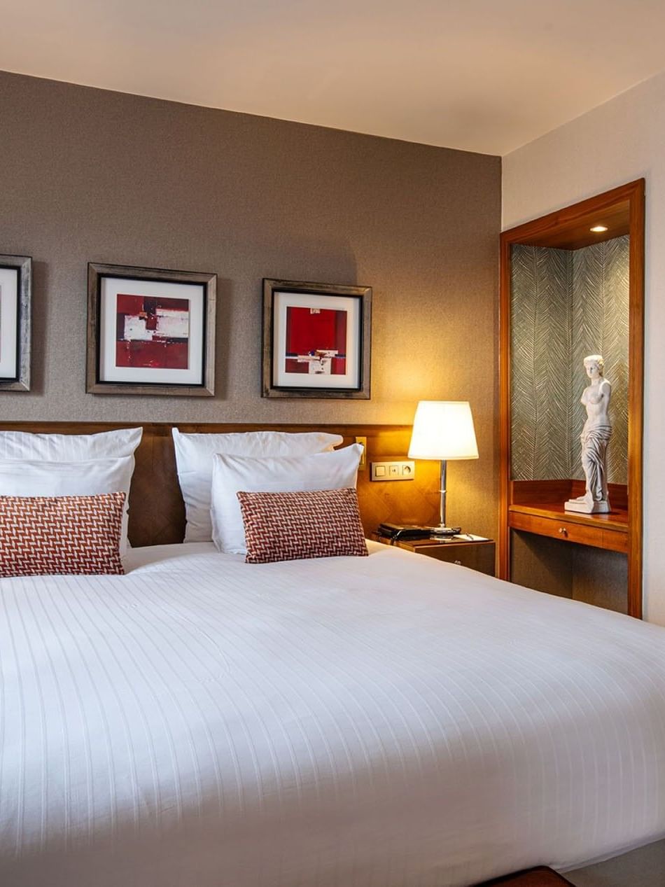 Bed between side tables near statue on a wooden stand in Warwick Suite at Warwick Grand Place Brussels