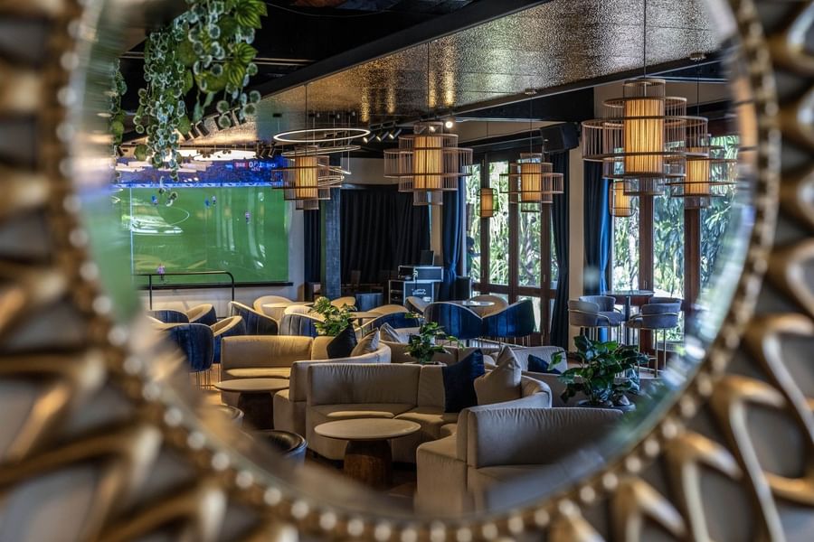 Grey sofas by round tables under cage pendant lights near a soccer screen in Hibiscus Lounge at Warwick Fiji Resort and Spa