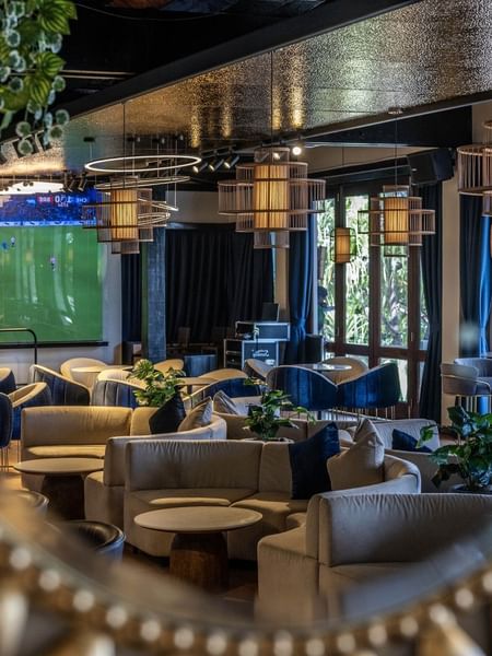 Grey sofas by round tables under cage pendant lights near a soccer screen in Hibiscus Lounge at Warwick Fiji Resort and Spa