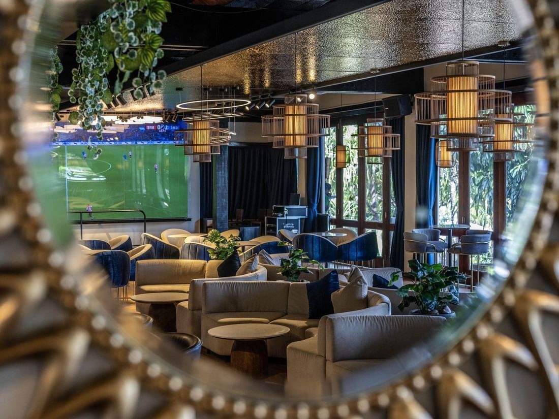 Grey sofas by round tables under cage pendant lights near a soccer screen in Hibiscus Lounge at Warwick Fiji Resort and Spa