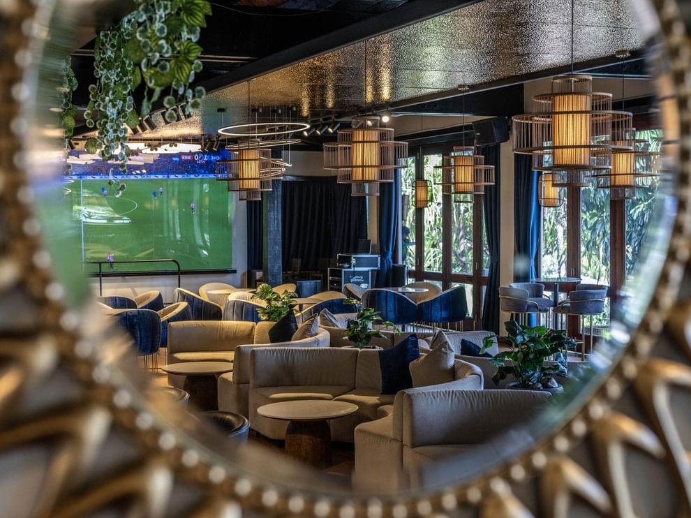 Grey sofas by round tables under cage pendant lights near a soccer screen in Hibiscus Lounge at Warwick Fiji Resort and Spa