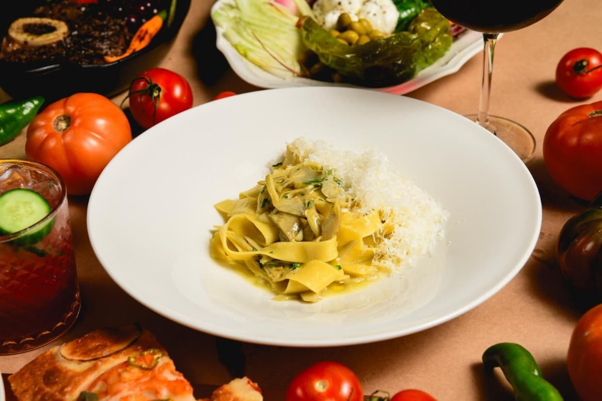 A plate of pasta with vegetables and cheese, accompanied by a glass of wine and other dishes.
