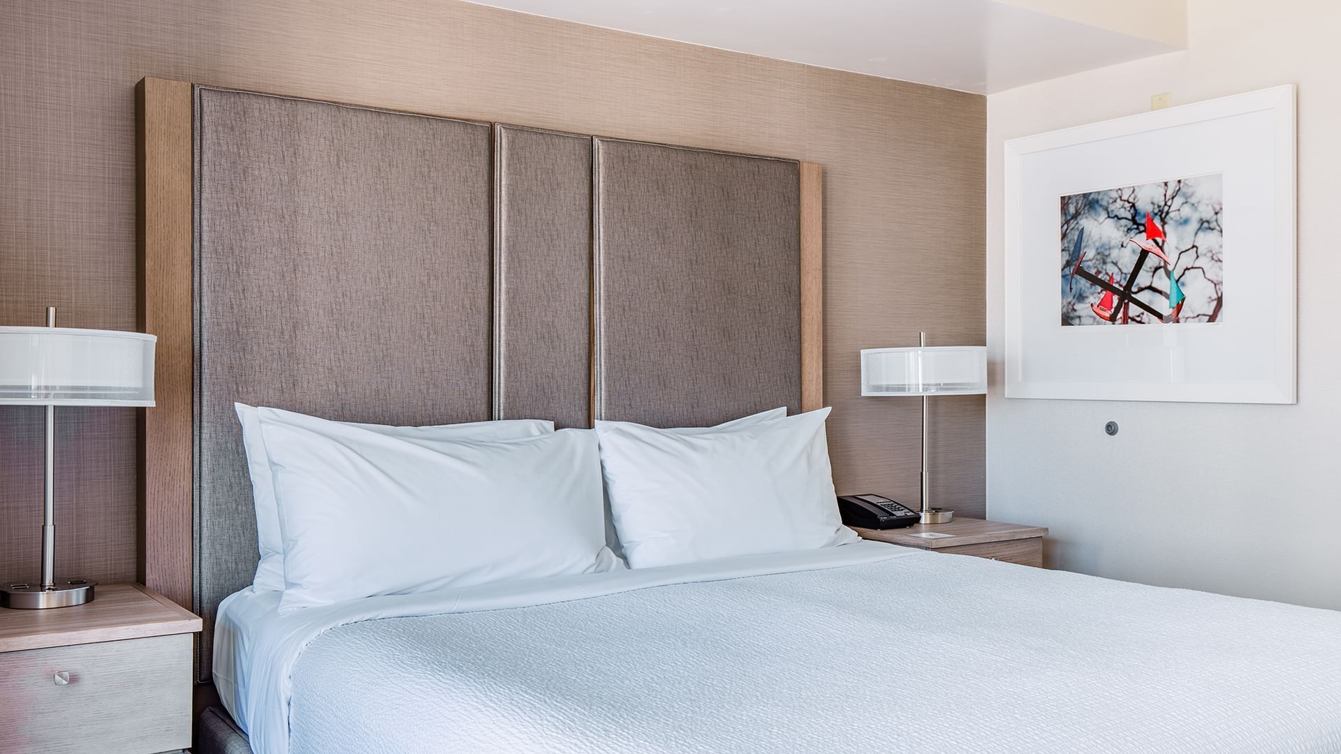 A hotel room with a king-sized bed, two nightstands, lamps, and artwork on the wall.