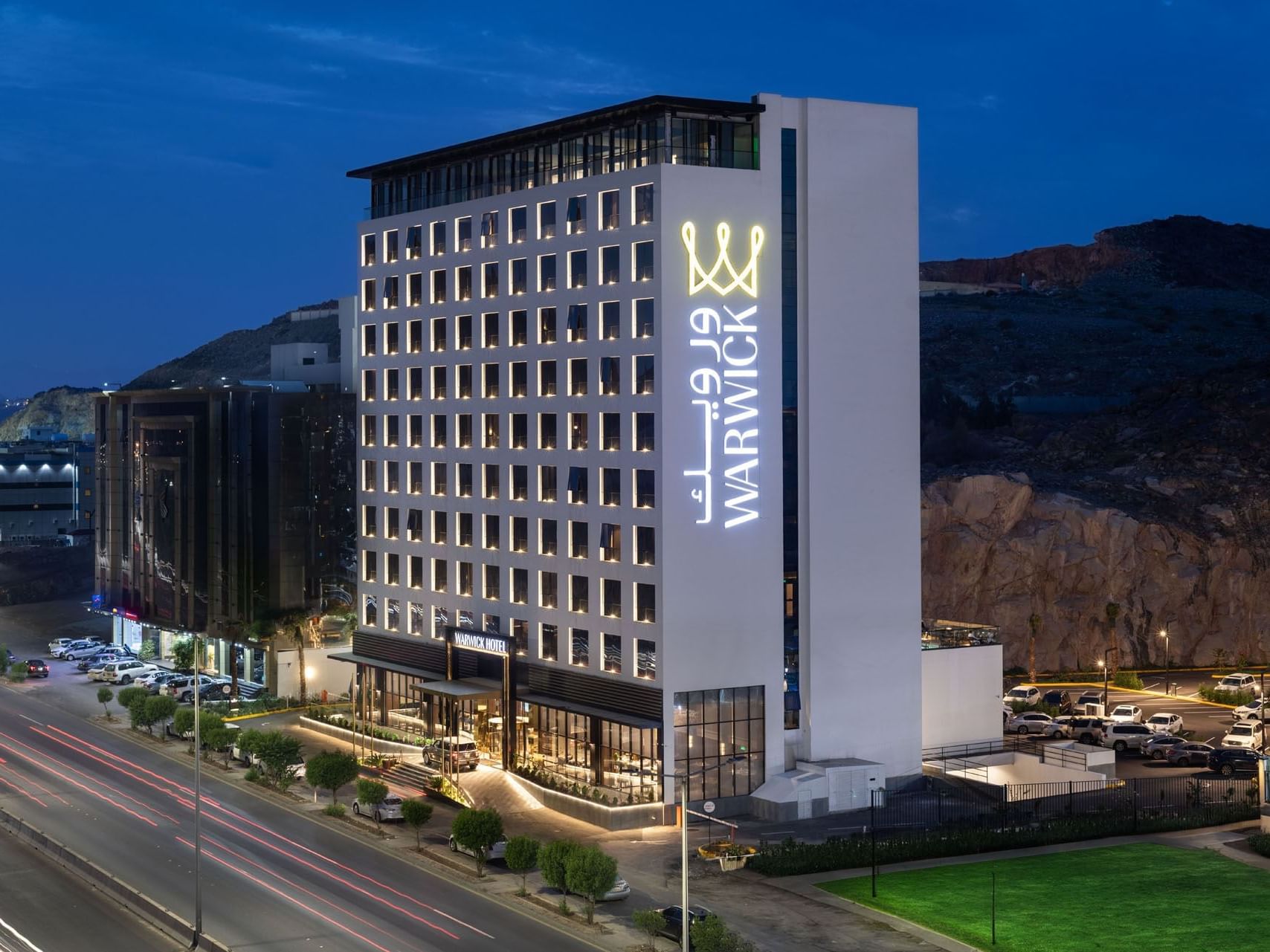 Exterior view of the Warwick Al Taif Hotel at night with illuminated signage and surrounding urban landscape