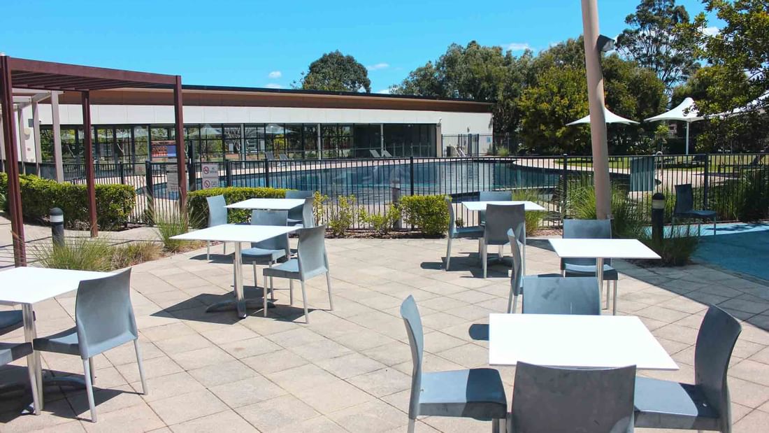 Outdoor seating area with tables and chairs near a fenced swimming pool at Mercure Kooindah Waters