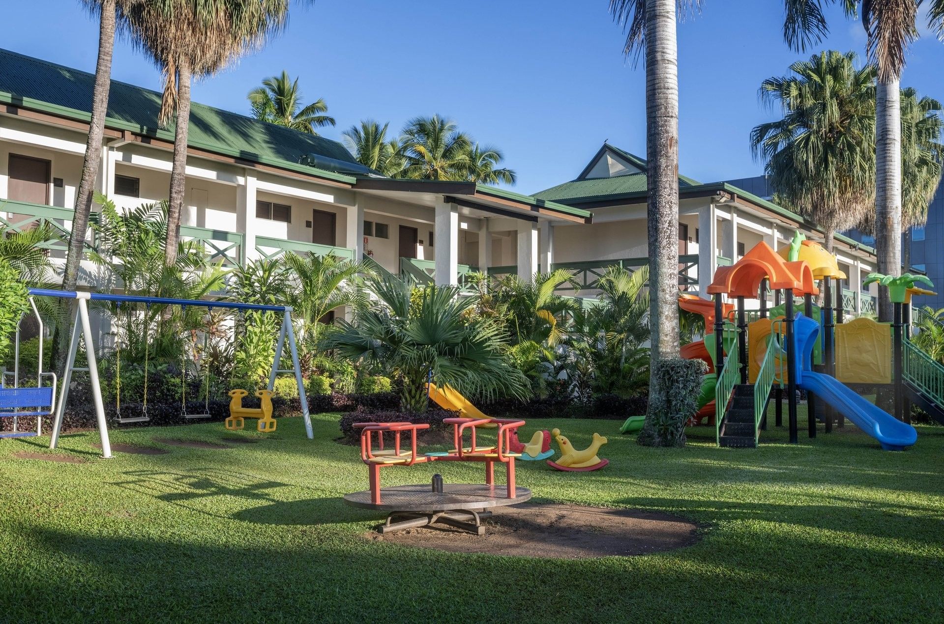 Colorful slides and swings on a green lawn by resort wings and palm trees at TokaToka Resort Nadi Fiji