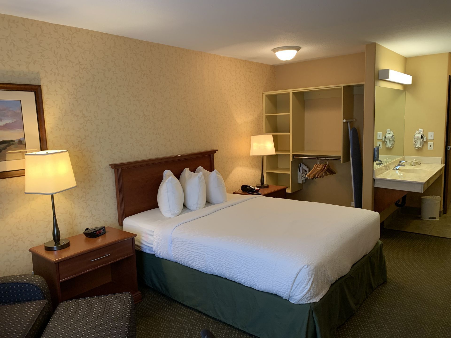 Queen bed with nightstands in Accessible room with carpeted floors at Merit Hotel & Suites