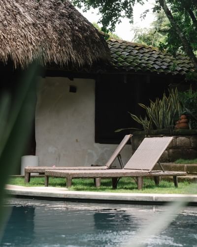 Tumbonas junto a la piscina bajo una cabaña con techo de paja en el tranquilo Morgan's Rock Reserve & Ecolodge.