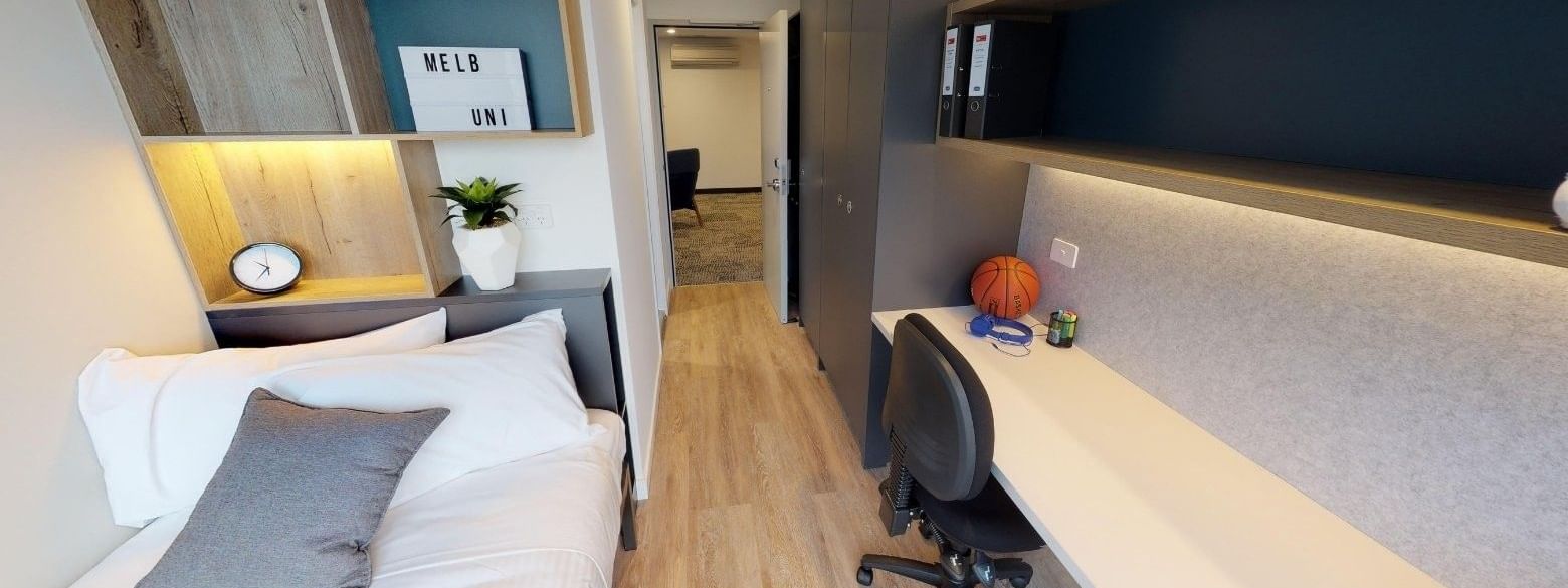 Modern bedroom with single bed, desk, chair, and basketball on desk in a dormitory.