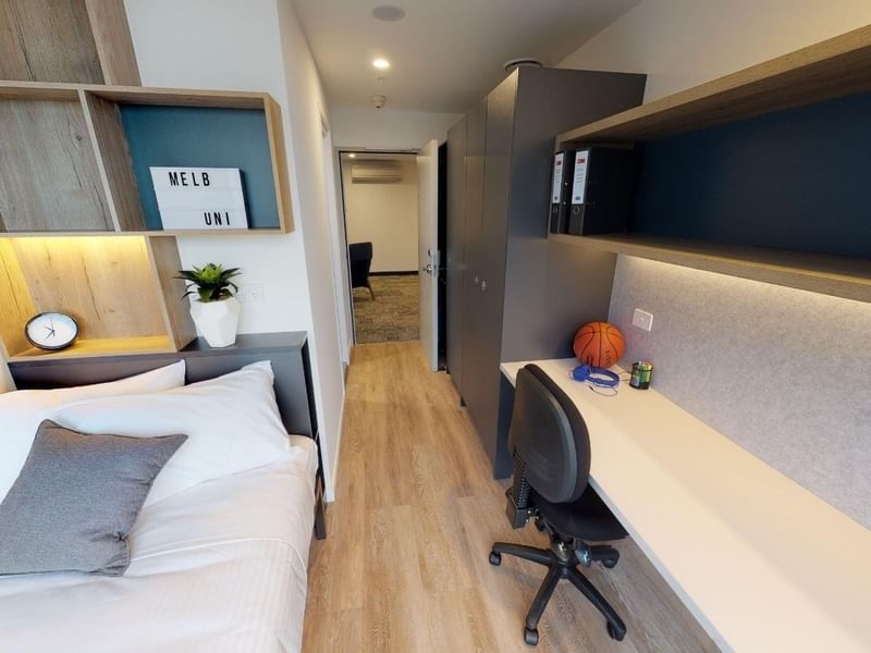 Modern bedroom with single bed, desk, chair, and basketball on desk in a dormitory.