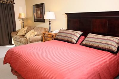 A well-lit hotel room with a King-sized bed, a small sofa, and lamps at The Pointe at Castle Hill