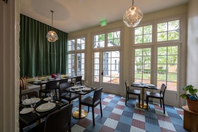 Bright dining room with dark wood tables, glass pendant lights, and patterned tile floor at The Ashbrook Hotel