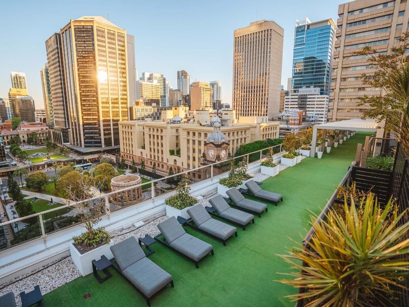 Rooftop garden with loungers overlooking a sunny cityscape in Soiree Deck at Sofitel Brisbane Central