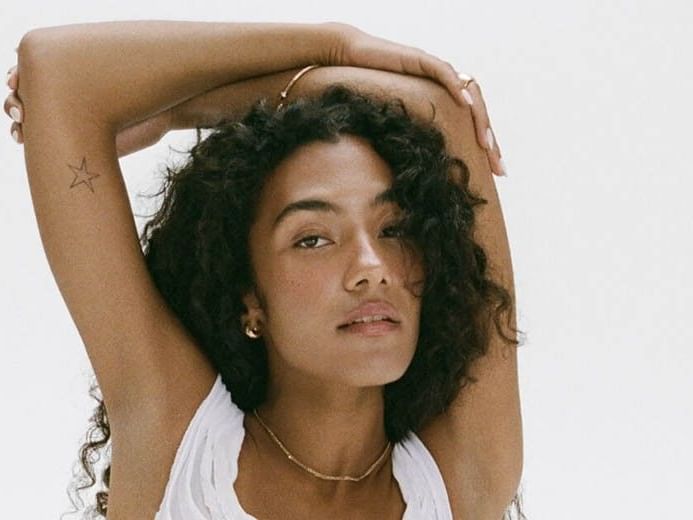 Olivia Dean poses with arms raised behind her head for The Art of Loving Tour 2026.