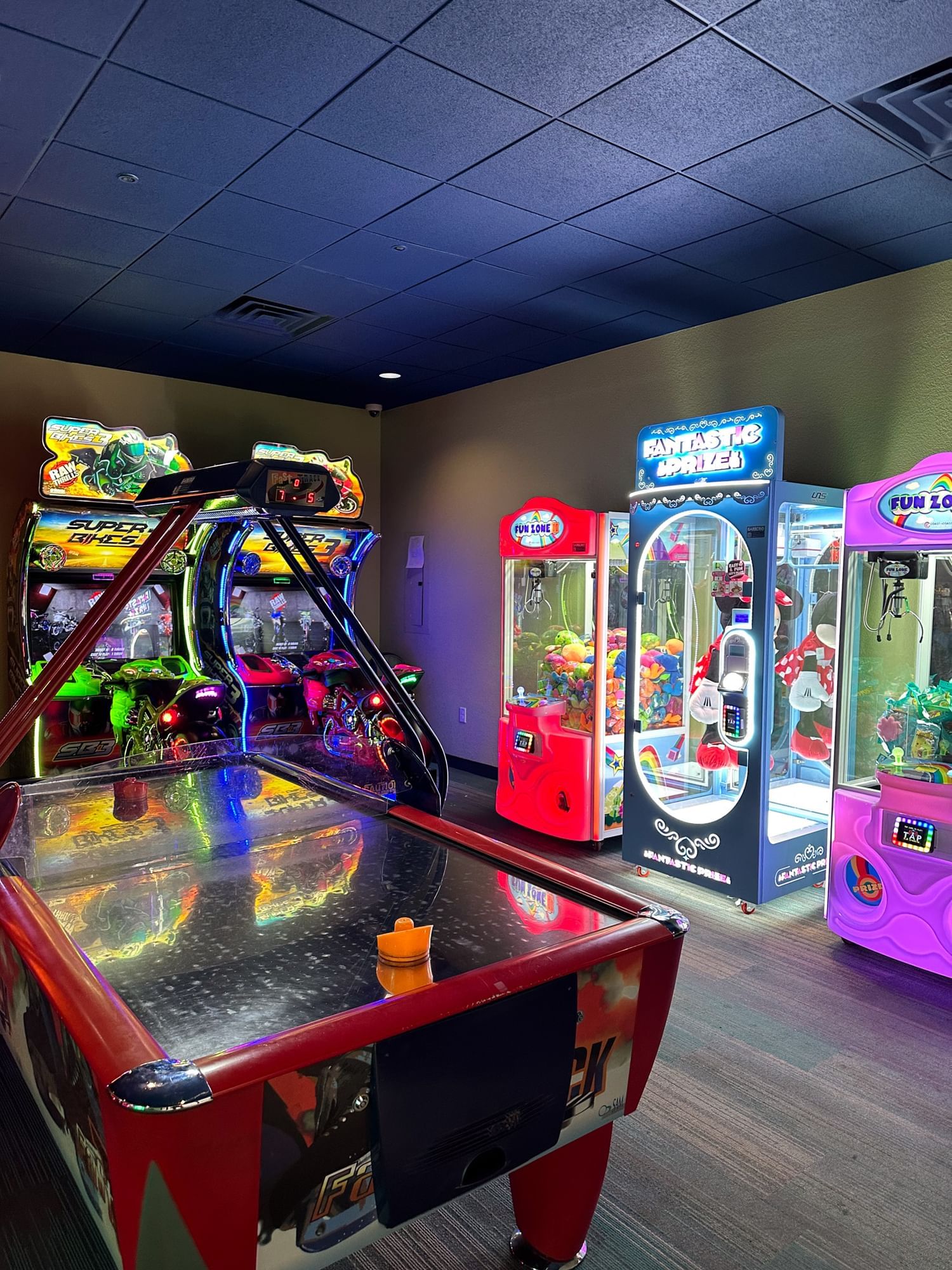 A close up shot of the Rosen Inn International video arcade in Orlando showing a air hockey table, two motorbike racing games and three crane games.