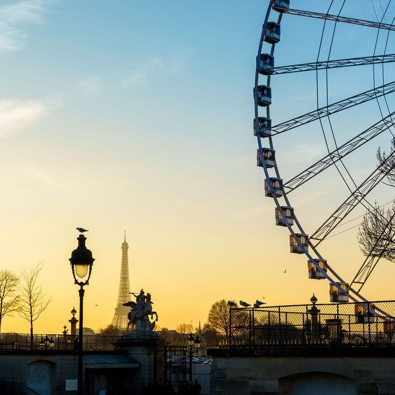Sunset view of Paris featuring the Eiffel Tower, a Ferris wheel, and silhouetted trees near Warwick Hotels and Resorts
