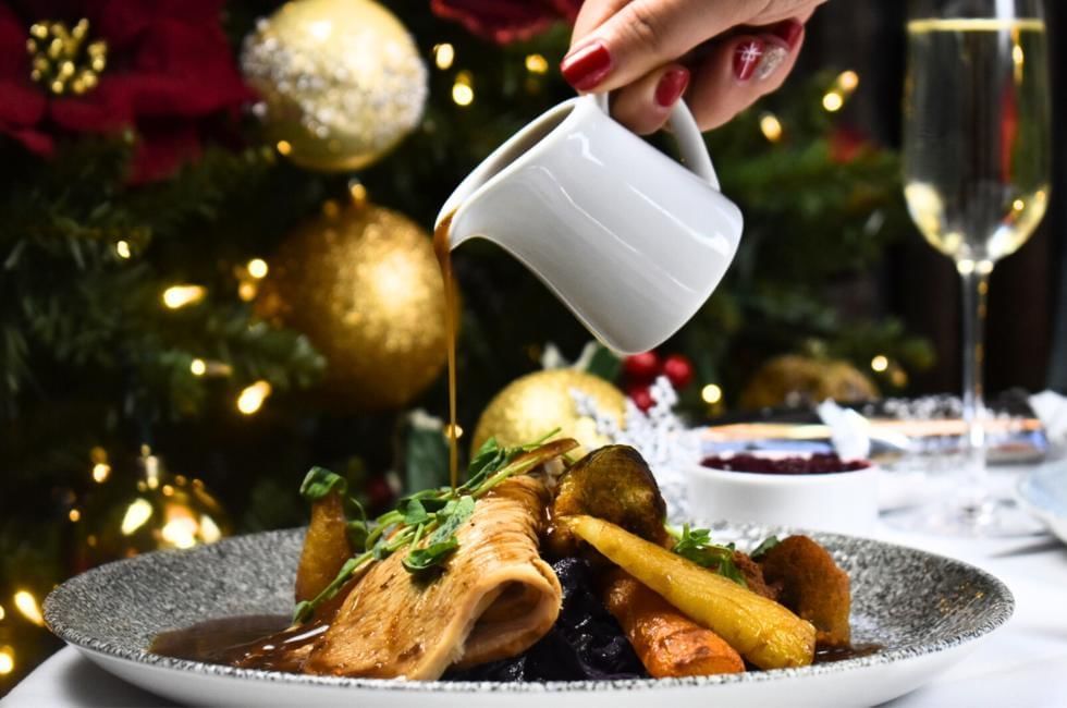 Person pouring gravy over festive lunch and dinner at Gorse Hill, Surrey