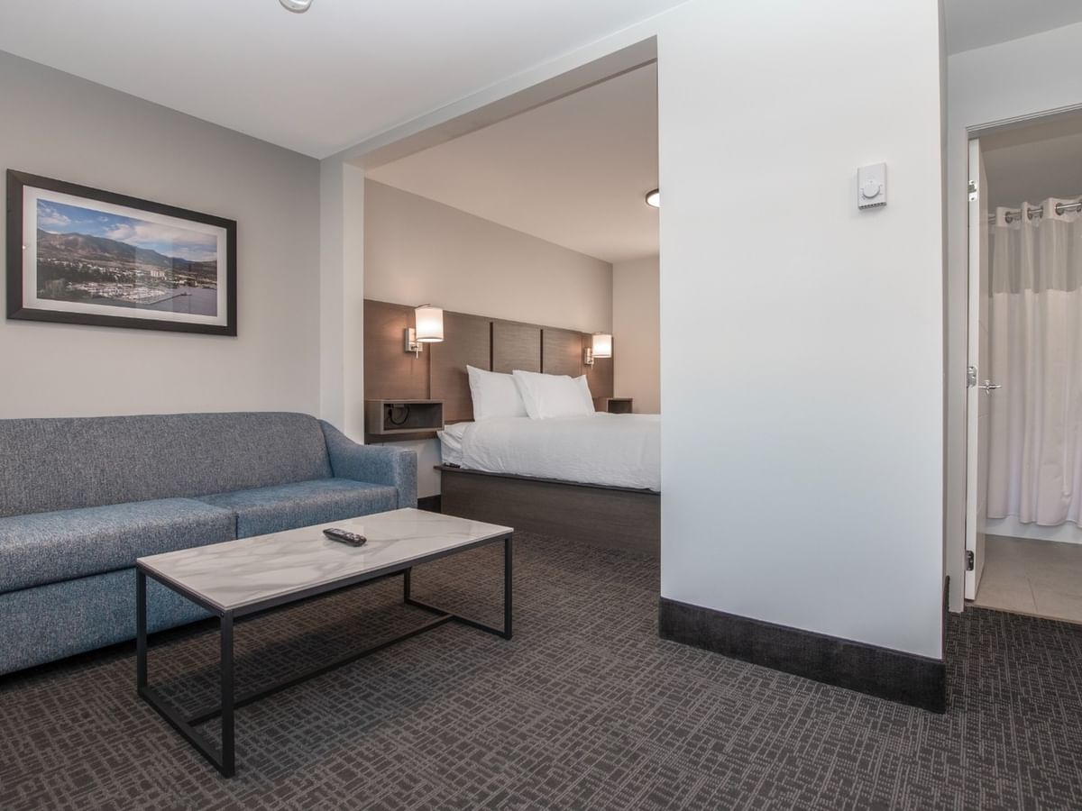 Hotel suite with couch, coffee table, and bedroom with bed and bathroom with toilet.