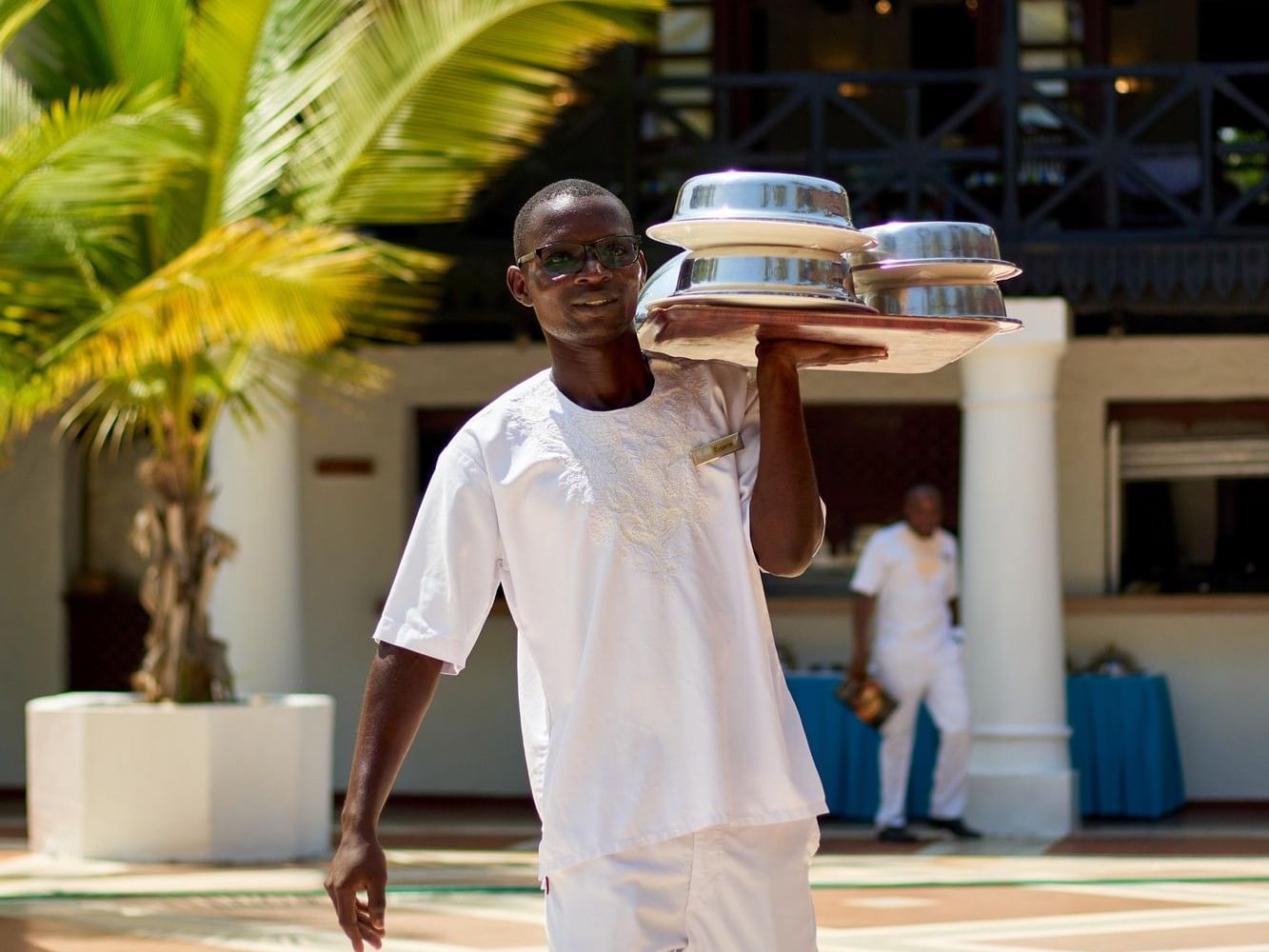 Staff member carrying room service trays on Serena Beach Resort & Spa grounds in Mombasa.
