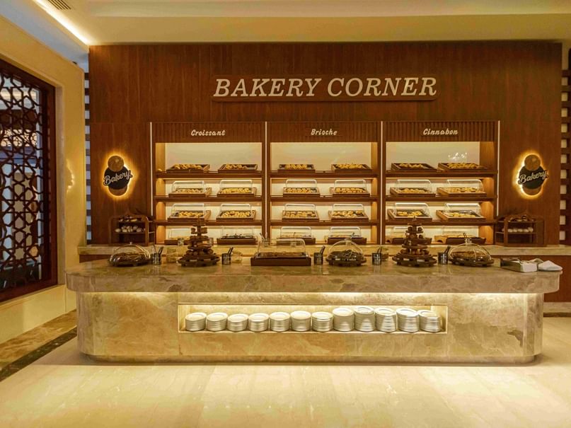 Bakery Corner display with croissant, brioche, and clafoutis trays, and a marble counter with stacked plates.