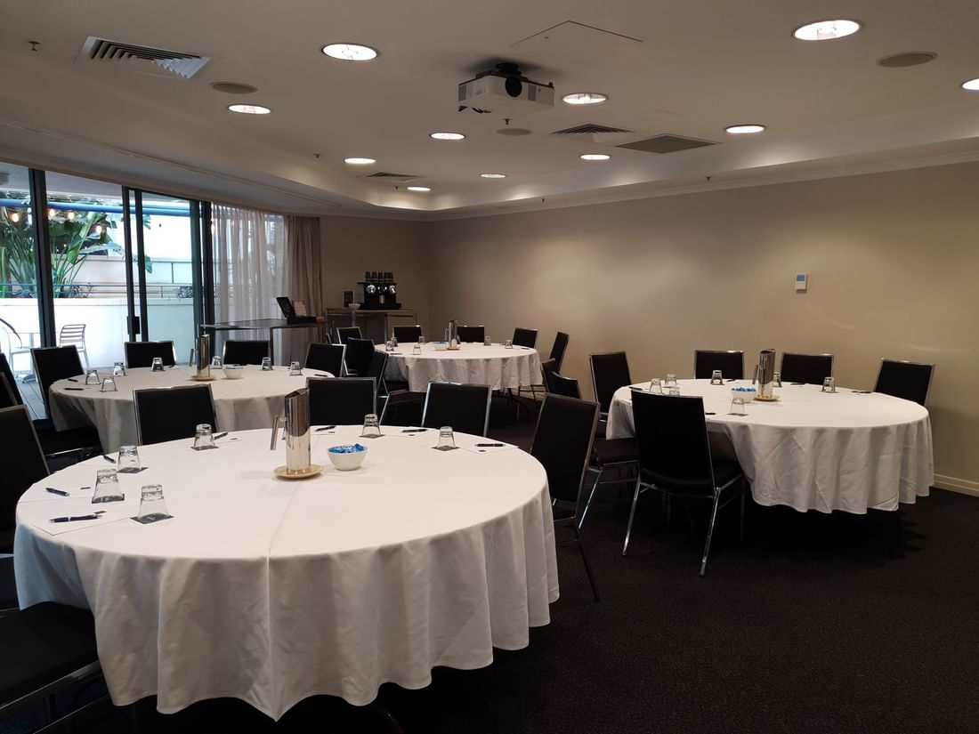 Albert Room 1 set up for a banquet with multiple round tables and a projector, opening to an outdoor at The Sebel Brisbane