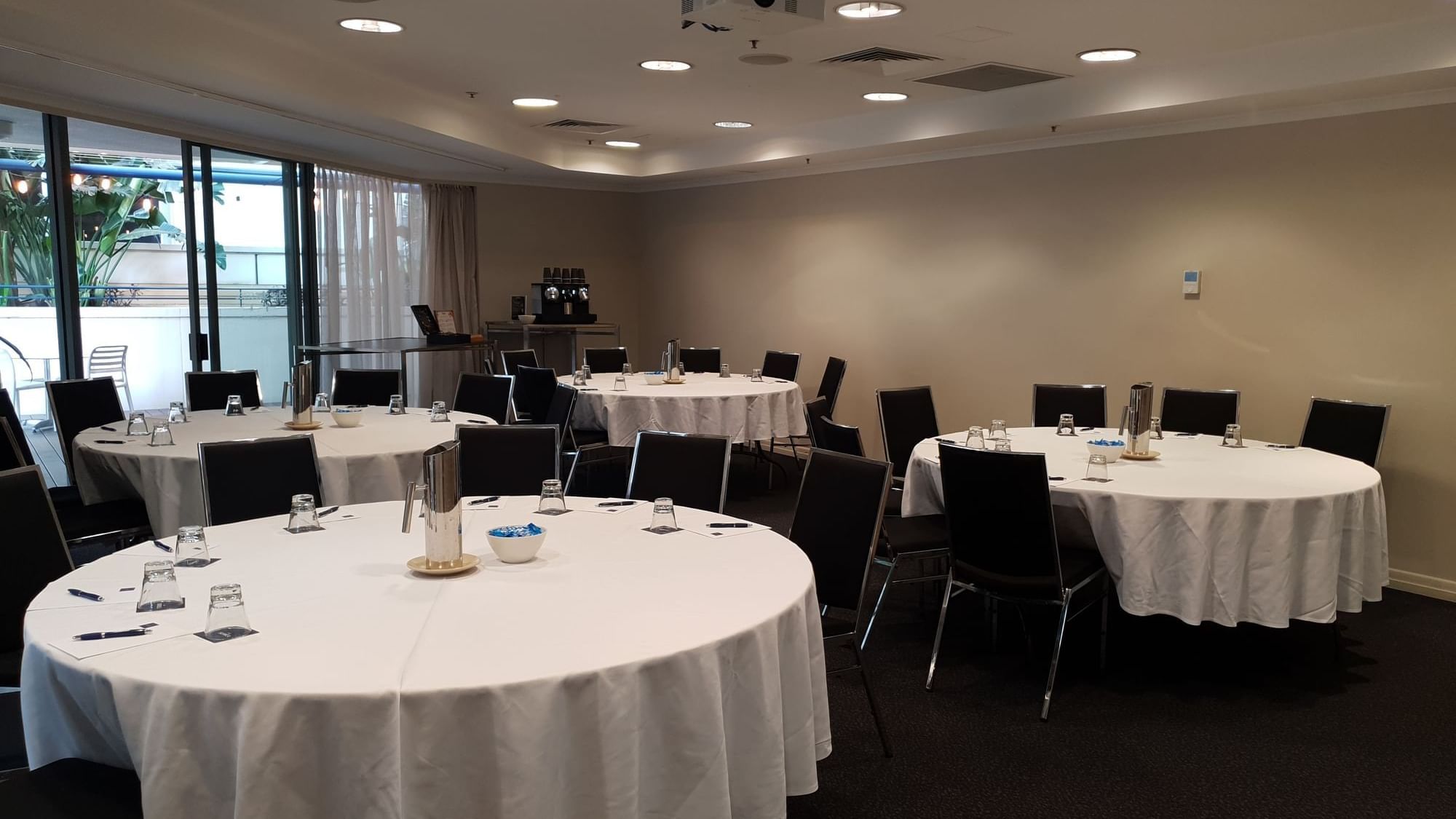 Albert Room 1 set up for a banquet with multiple round tables and a projector, opening to an outdoor at The Sebel Brisbane
